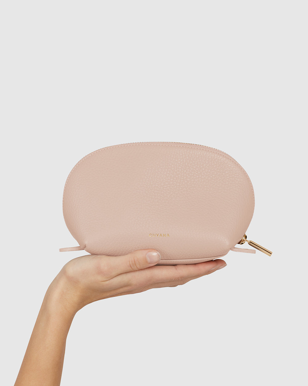 A hand holds a small oval pouch with a zipper on top.