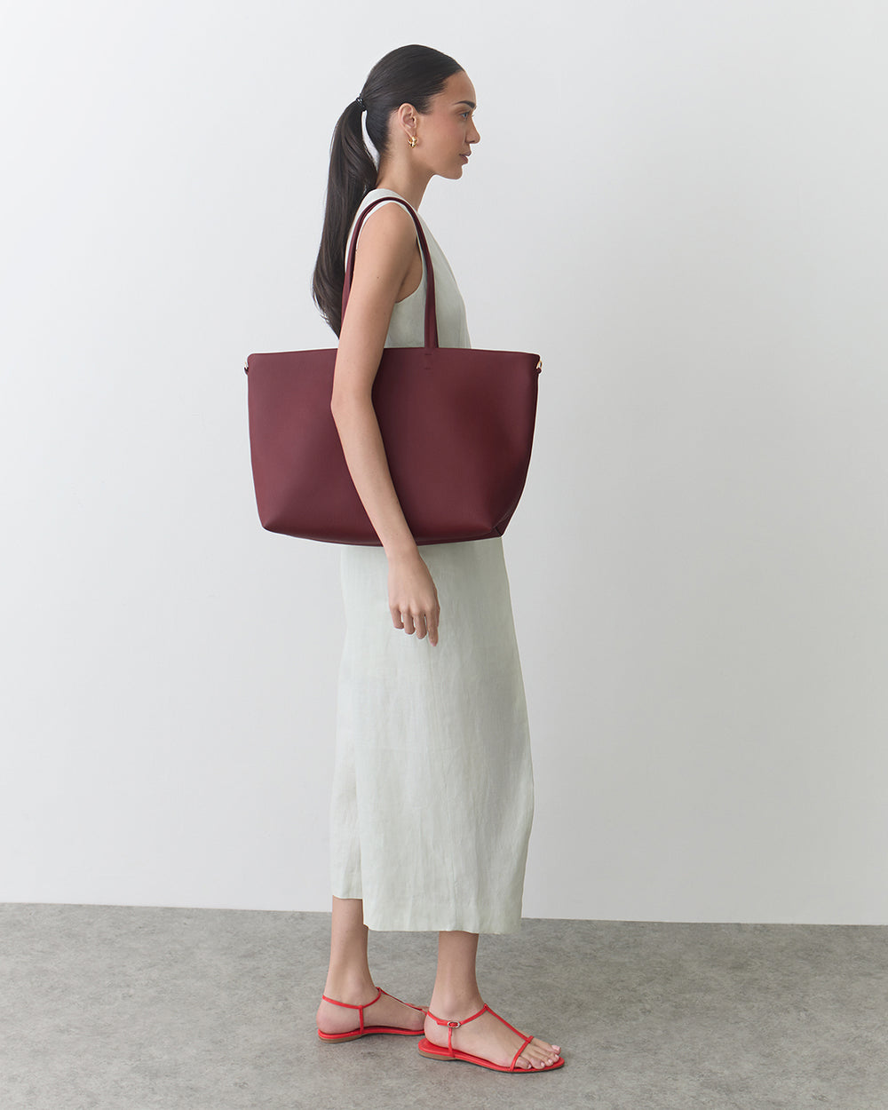 Person in a dress holding a large tote bag, wearing sandals.