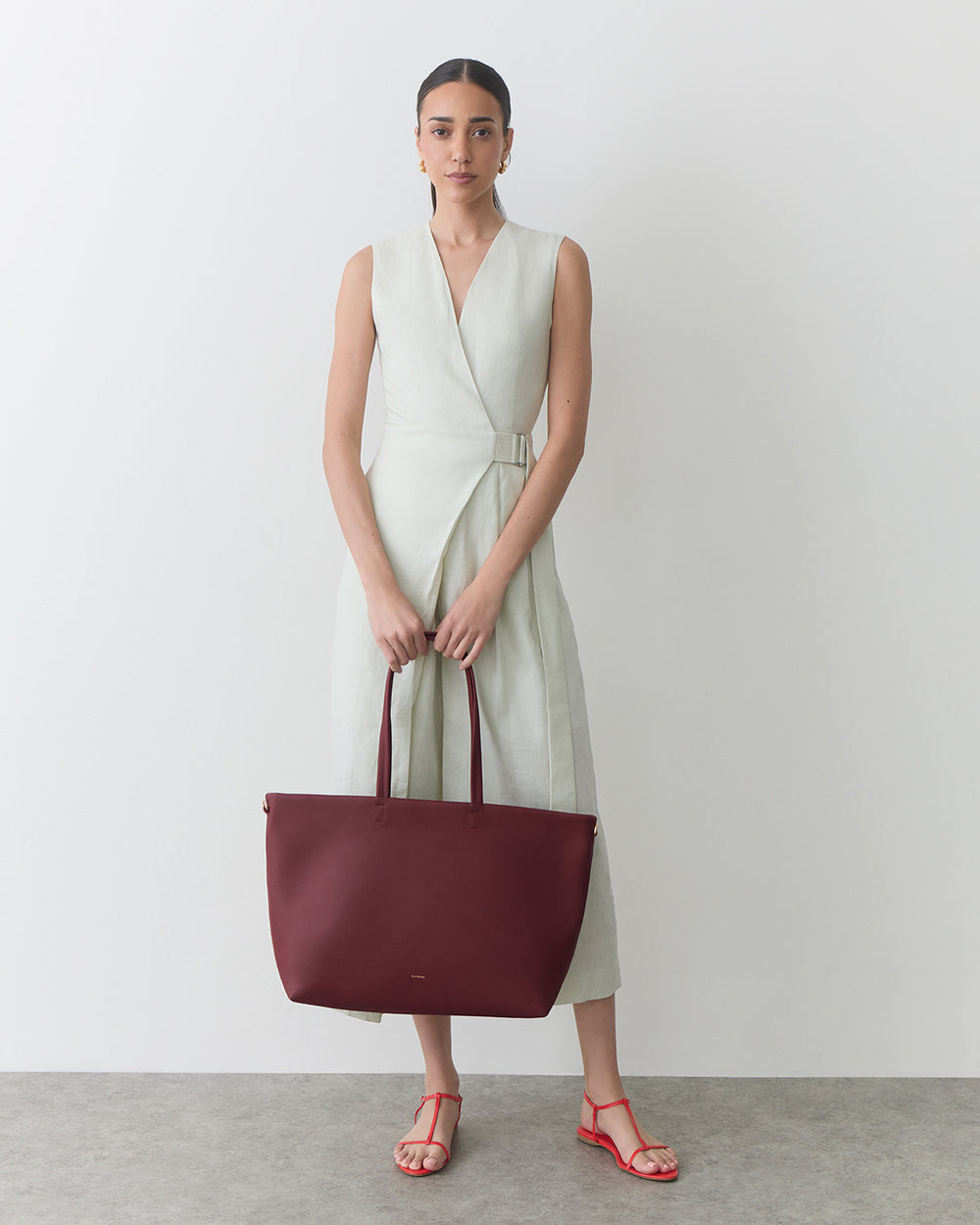 Person in a sleeveless dress holding a large tote bag.