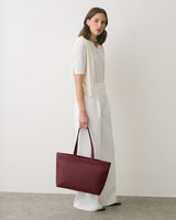 A person standing with a tote bag and wearing a light top and pants.