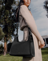 Person outdoors holding a handbag over their shoulder.