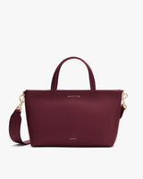 A handbag with a top handle, shoulder strap, and small gold embossed text.