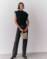 Person holding small handbag wearing sleeveless top and jeans standing indoors.