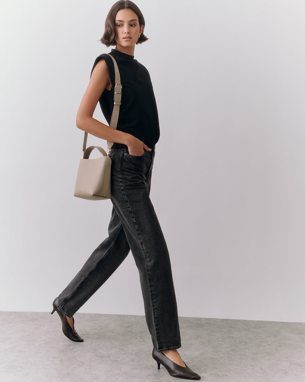 A person walking with a handbag, wearing a sleeveless top and pants.