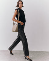 A person walking with a handbag, wearing a sleeveless top and pants.