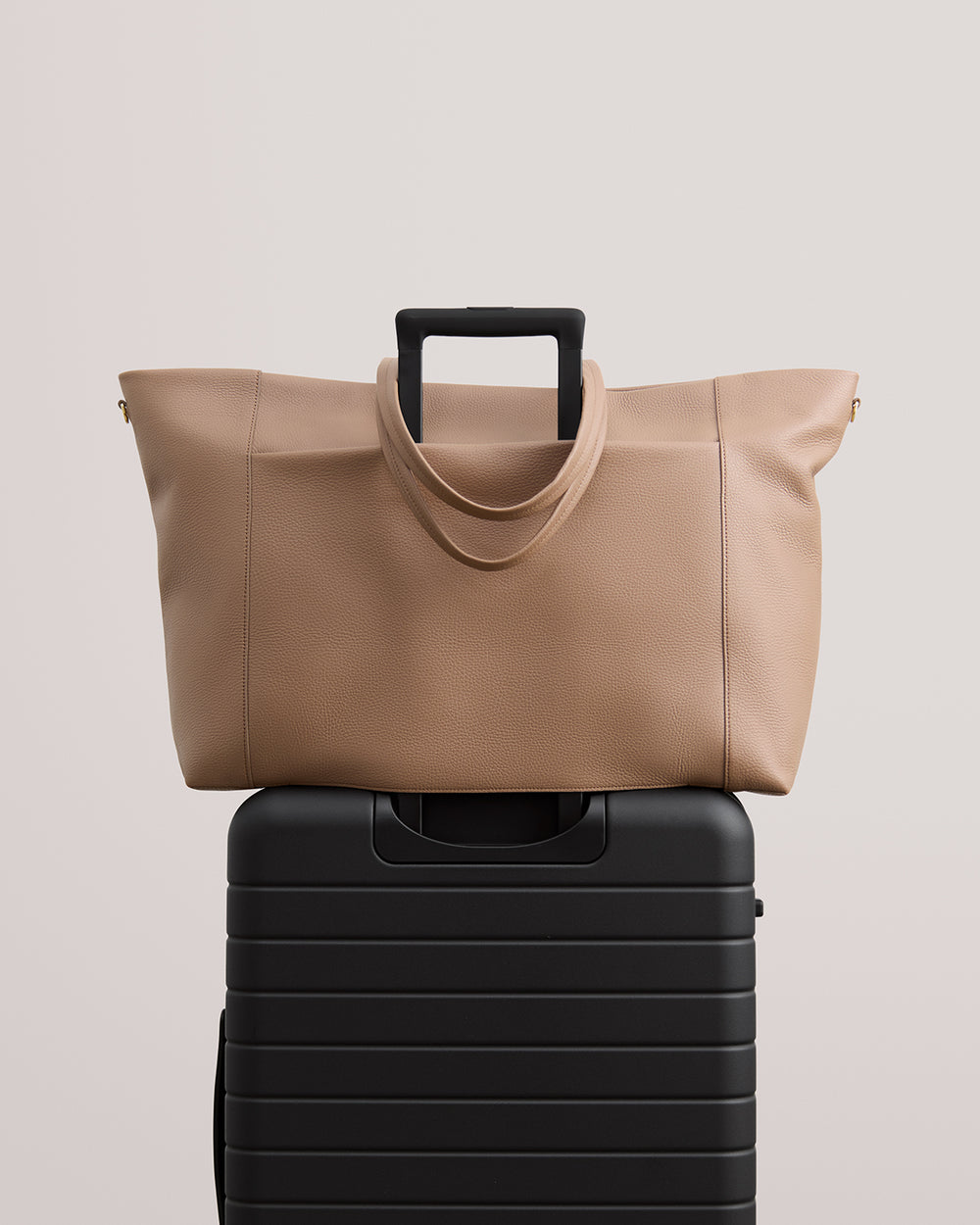 Travel bag with a luggage sleeve placed on top of a suitcase with extended handle