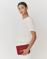 Person holding a slim clutch against their side standing against a light background.