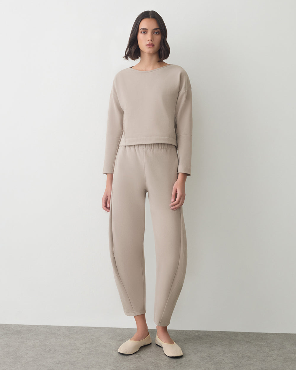 Person wearing a matching long-sleeve top and pants with slip-on shoes standing indoors.