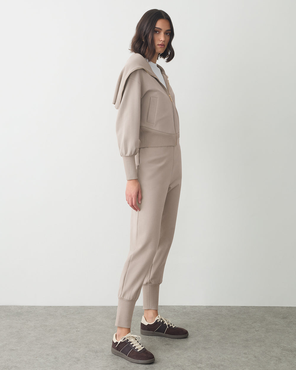 Person wearing a matching jacket and pants set with sneakers, standing sideways.