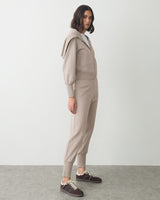 Person wearing a matching jacket and pants set with sneakers, standing sideways.