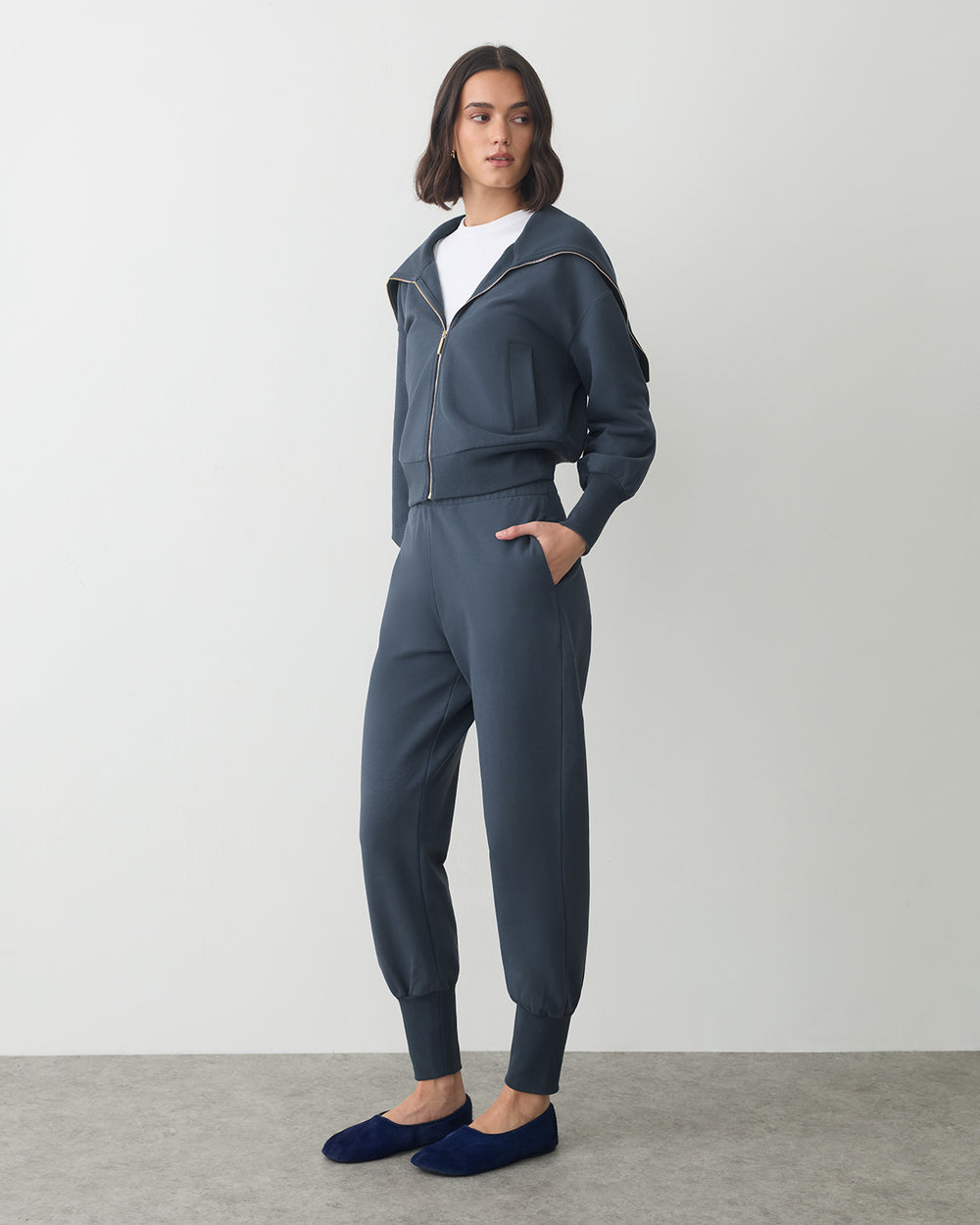 Person wearing a zip-up jacket, pants, and slip-on shoes, looking to the side.