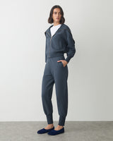 Person wearing a zip-up jacket, pants, and slip-on shoes, looking to the side.