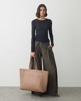 Person in long-sleeved top holds large travel bag and stands on gray floor.