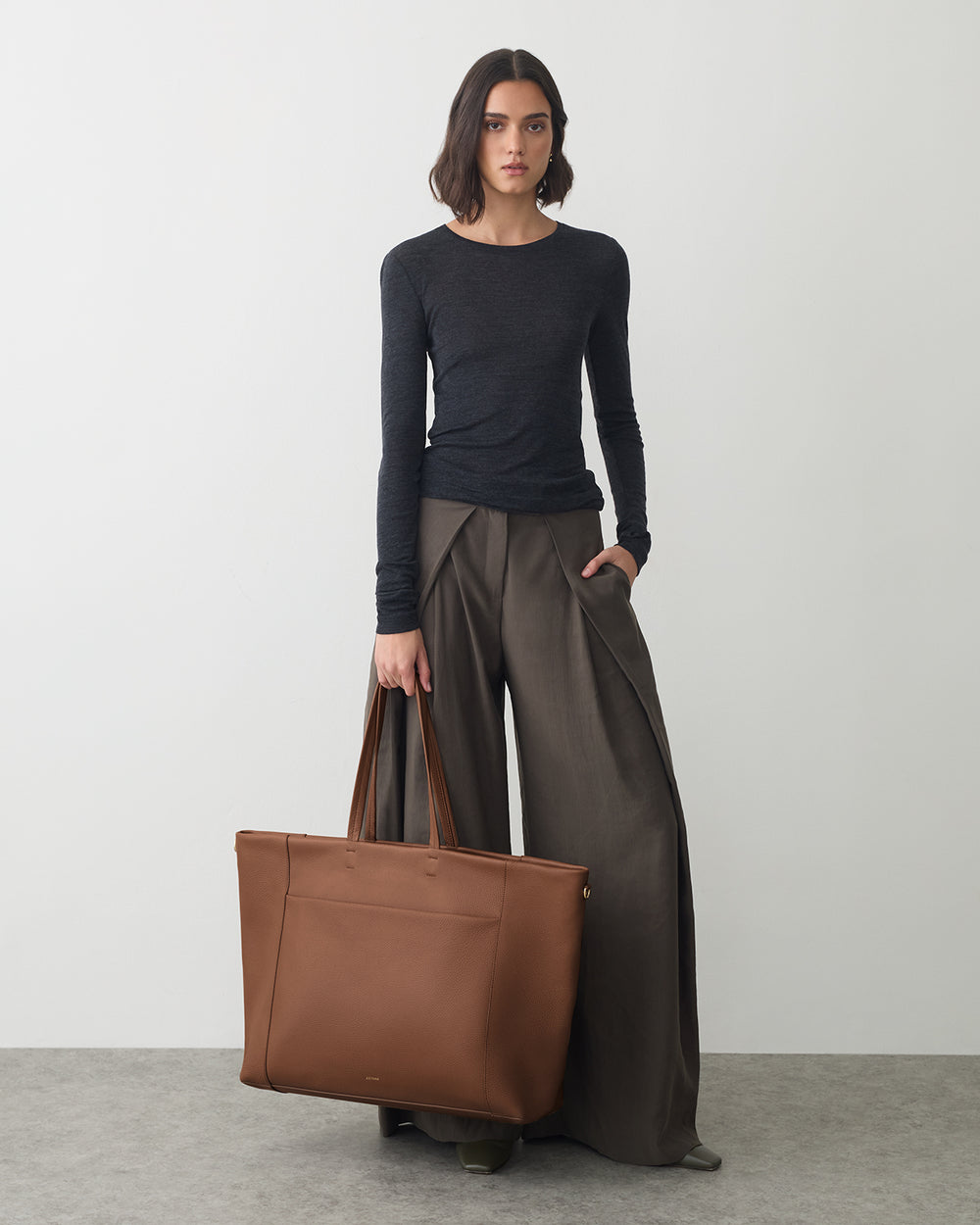 Person in long-sleeve top and wide-legged pants holding large tote bag.