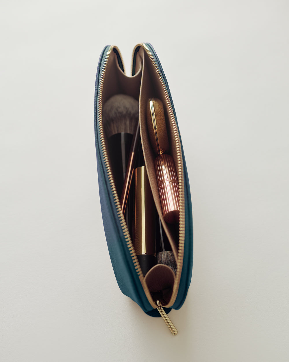 Makeup brushes and lipstick inside an open zippered cosmetic bag.