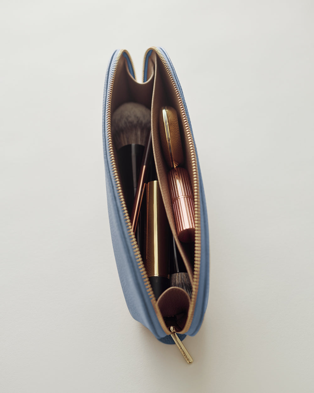 Makeup bag filled with brushes and lipstick viewed from above.