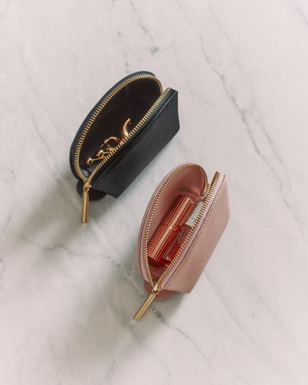 Two small zippered pouches on a marble surface, each holding cosmetic products.