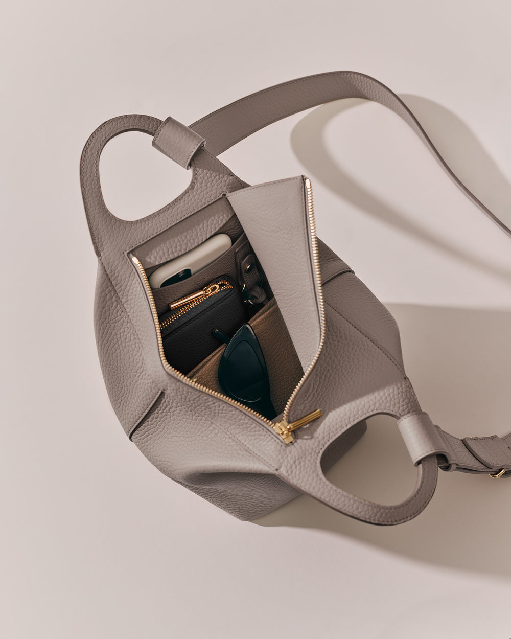 Open handbag with items like a phone, wallet, and sunglasses visible inside