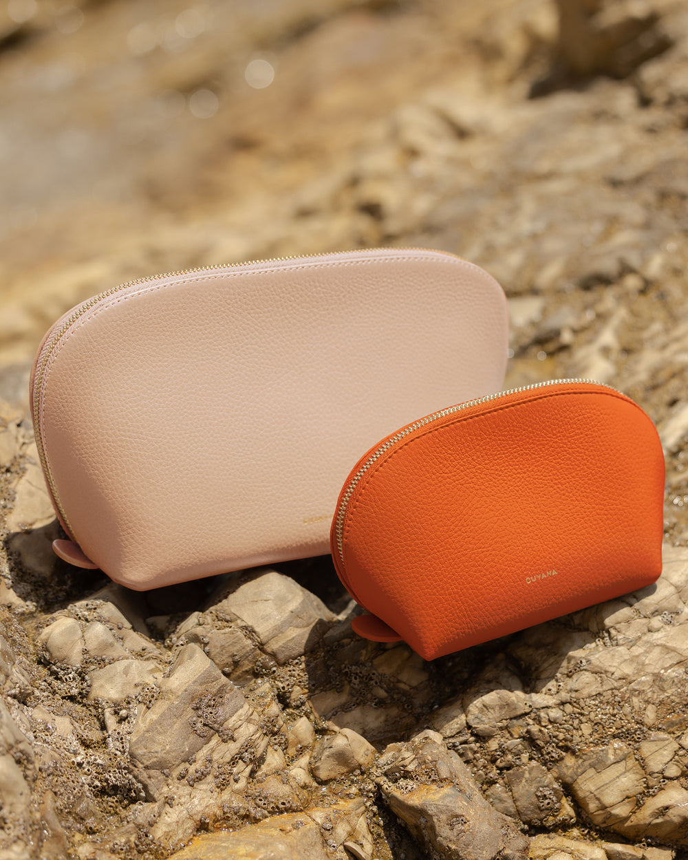 Two makeup pouches on a rocky surface outdoors.