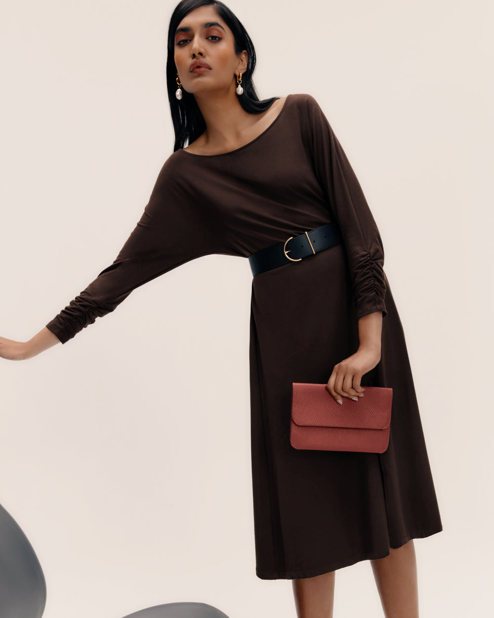 Person in dress with belt, holding a clutch in one hand, slightly leaning.