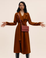 Person wearing long coat, holding arms out, with small bag across shoulder.