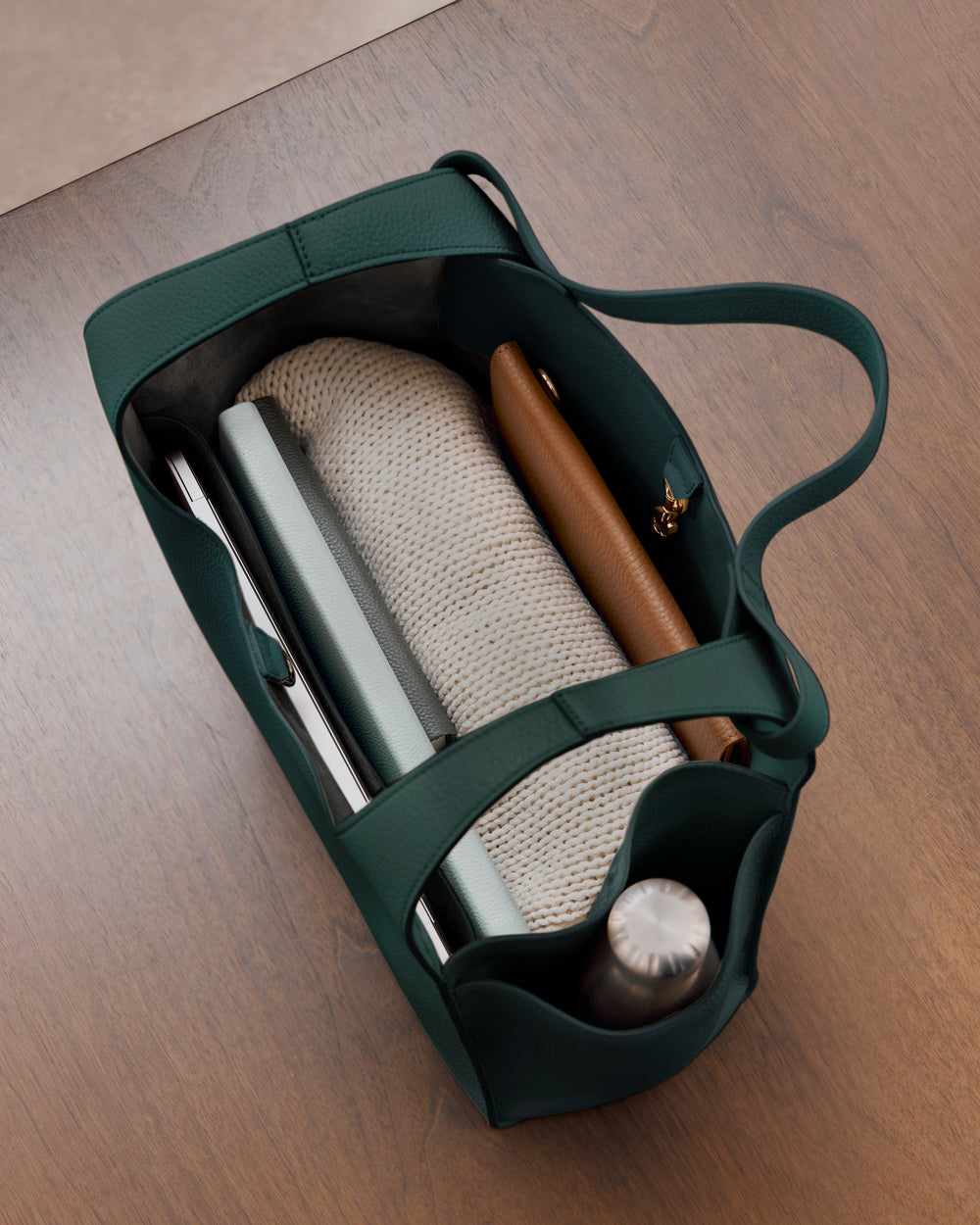 Open bag on table with books, a bottle, and a rolled-up item inside.