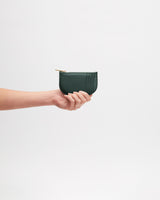 Hand holding a small zippered leather pouch against a plain background.