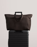Travel bag resting on a wheeled suitcase against a plain background.