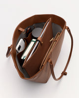Open tote bag with a book, phone, cup, and a folder inside.