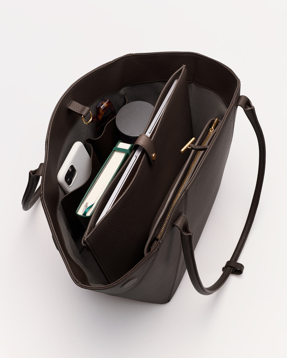 Open tote bag with phone, book, notebook, pen inside and straps visible.