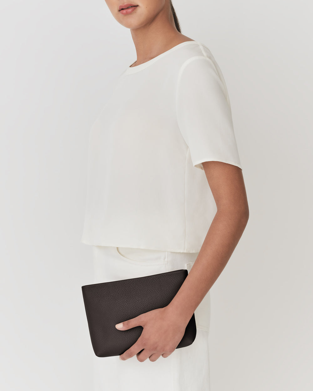 Person holding a small clutch bag under arm, with short-sleeve shirt and skirt.
