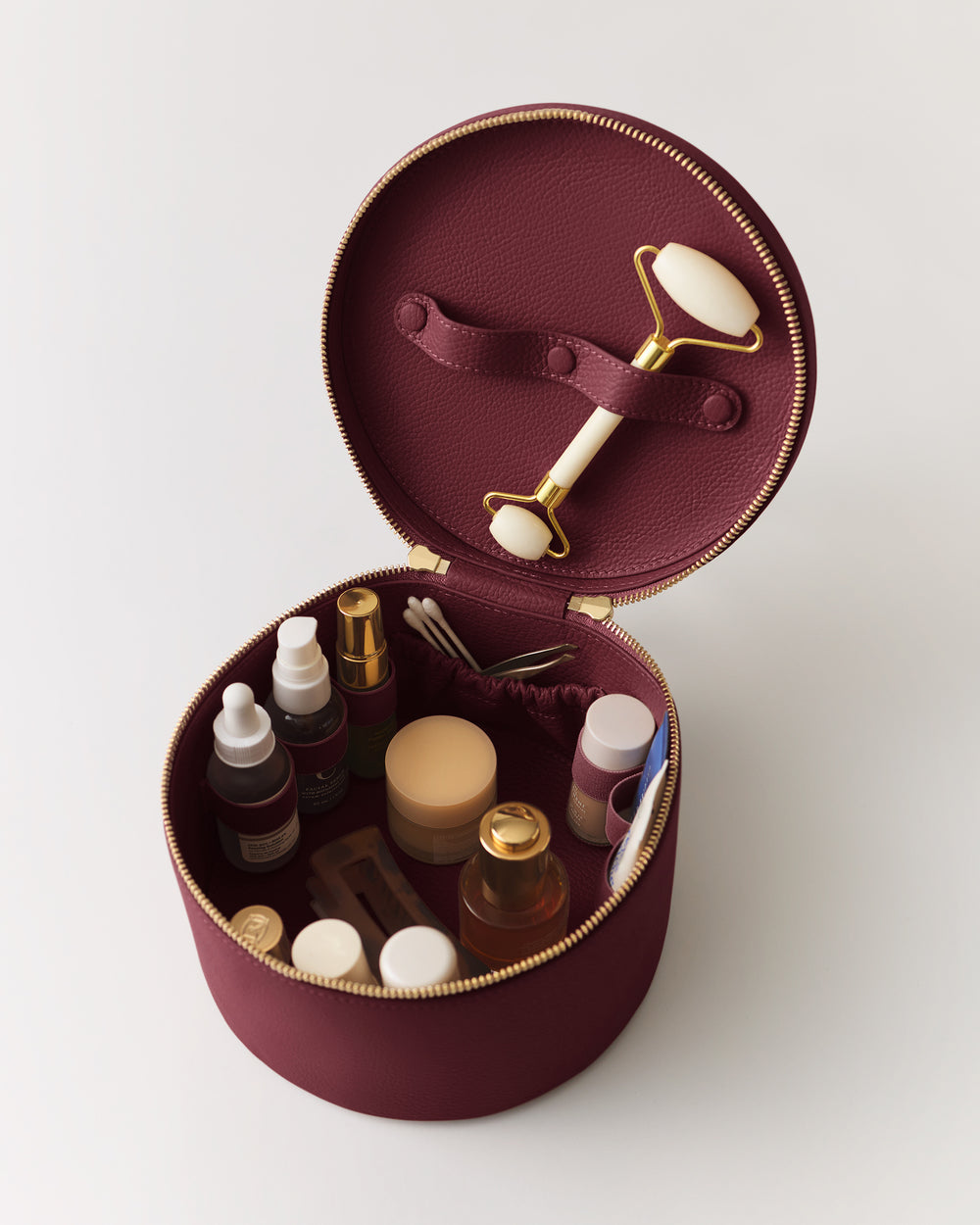 Round makeup case with skincare products and facial roller inside.