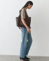 Person standing with a fringed tote bag, wearing jeans and ankle boots.