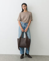 Person holding a fringed tote bag wearing a t-shirt, jeans, and ankle boots.