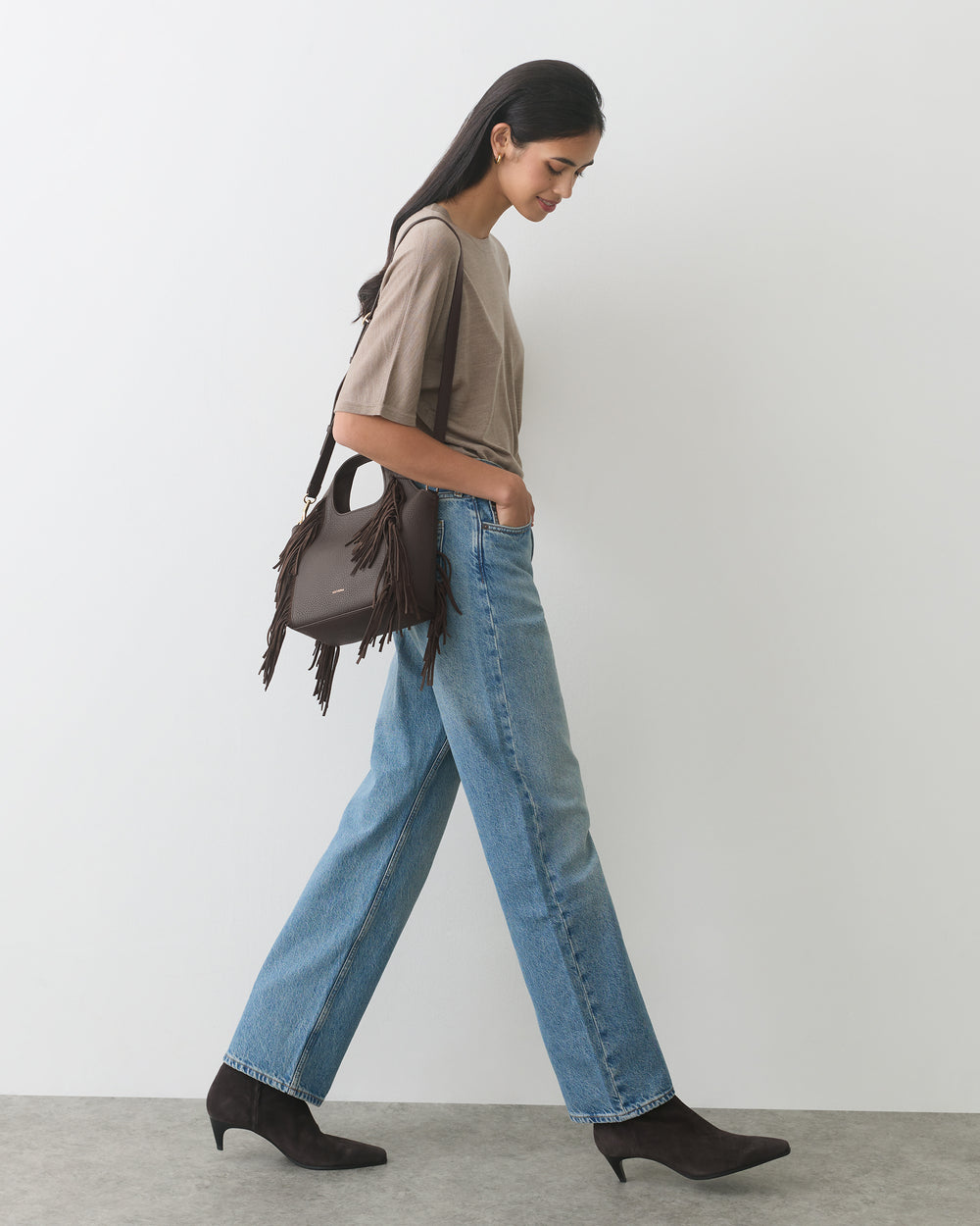 Person walking with a fringed shoulder bag, wearing a casual outfit and boots.
