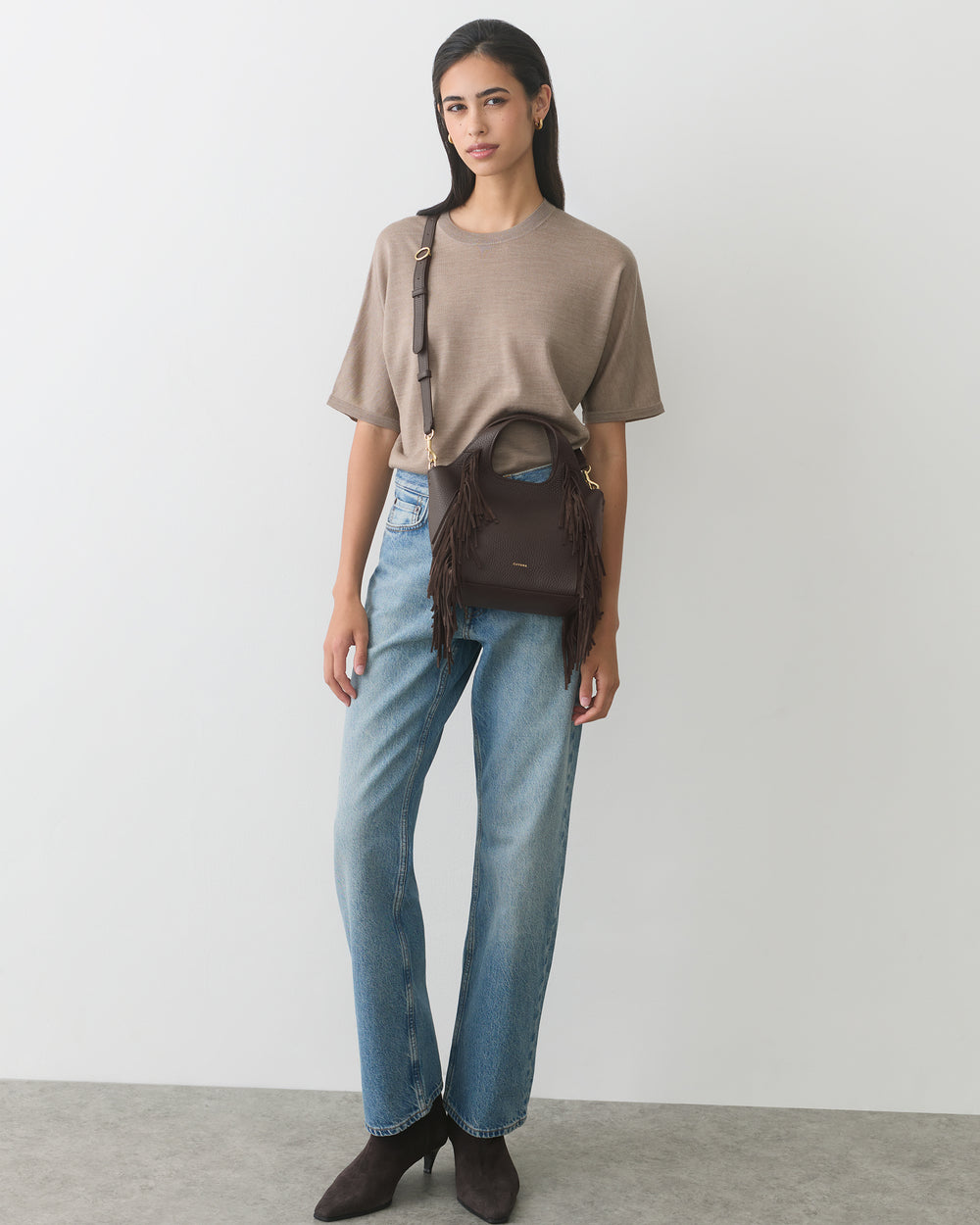 Person standing with fringed handbag and wearing casual outfit.
