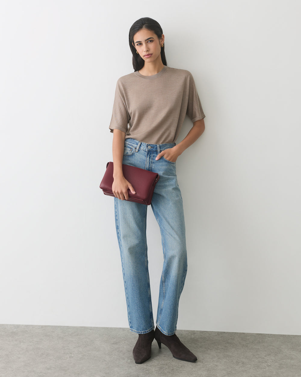 Person in casual outfit holding a clutch, standing against plain backdrop.