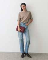 Person in casual outfit holding a clutch, standing against plain backdrop.
