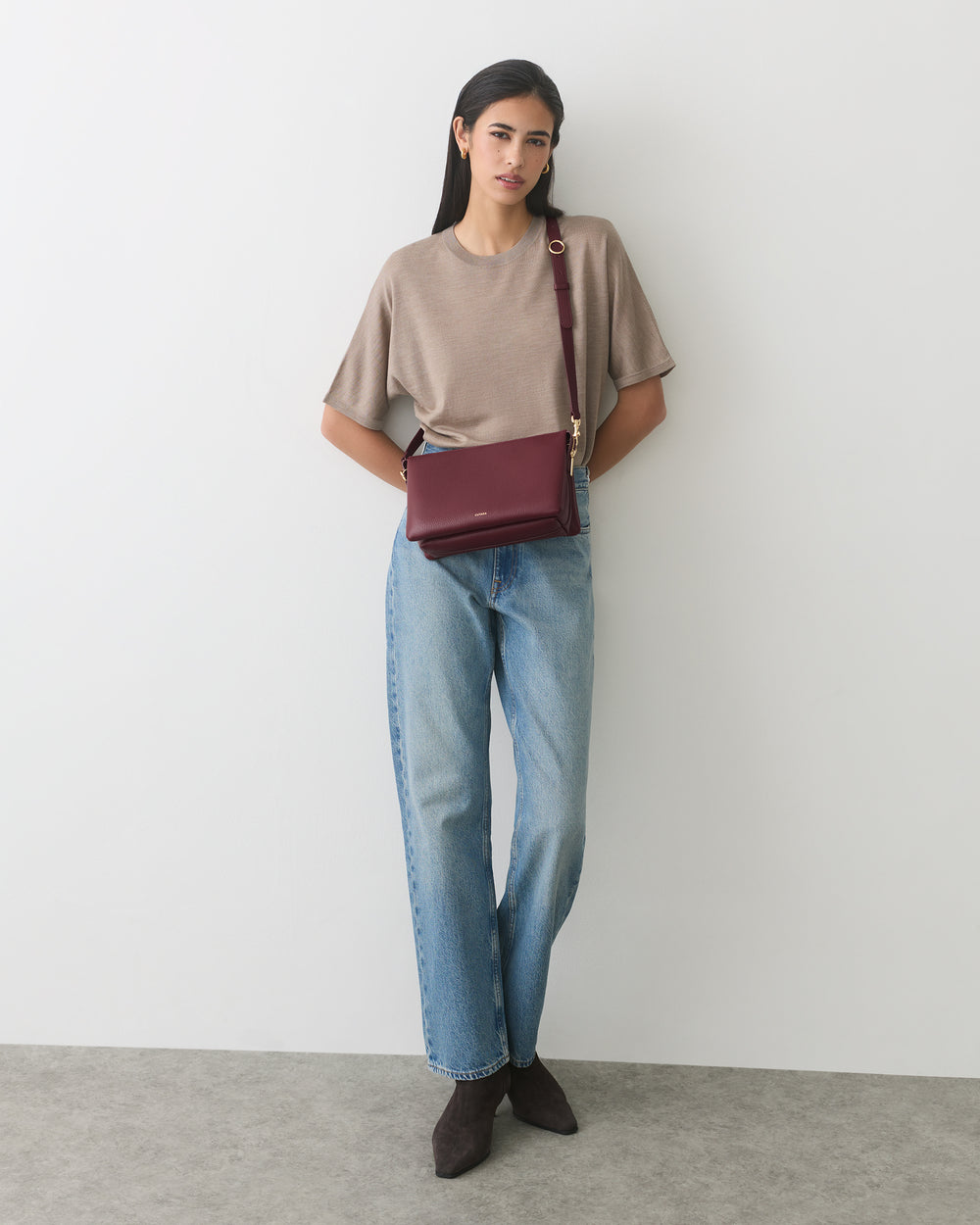 Person wearing a short-sleeve top and jeans, holding a shoulder bag.