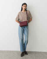 Person wearing a short-sleeve top and jeans, holding a shoulder bag.