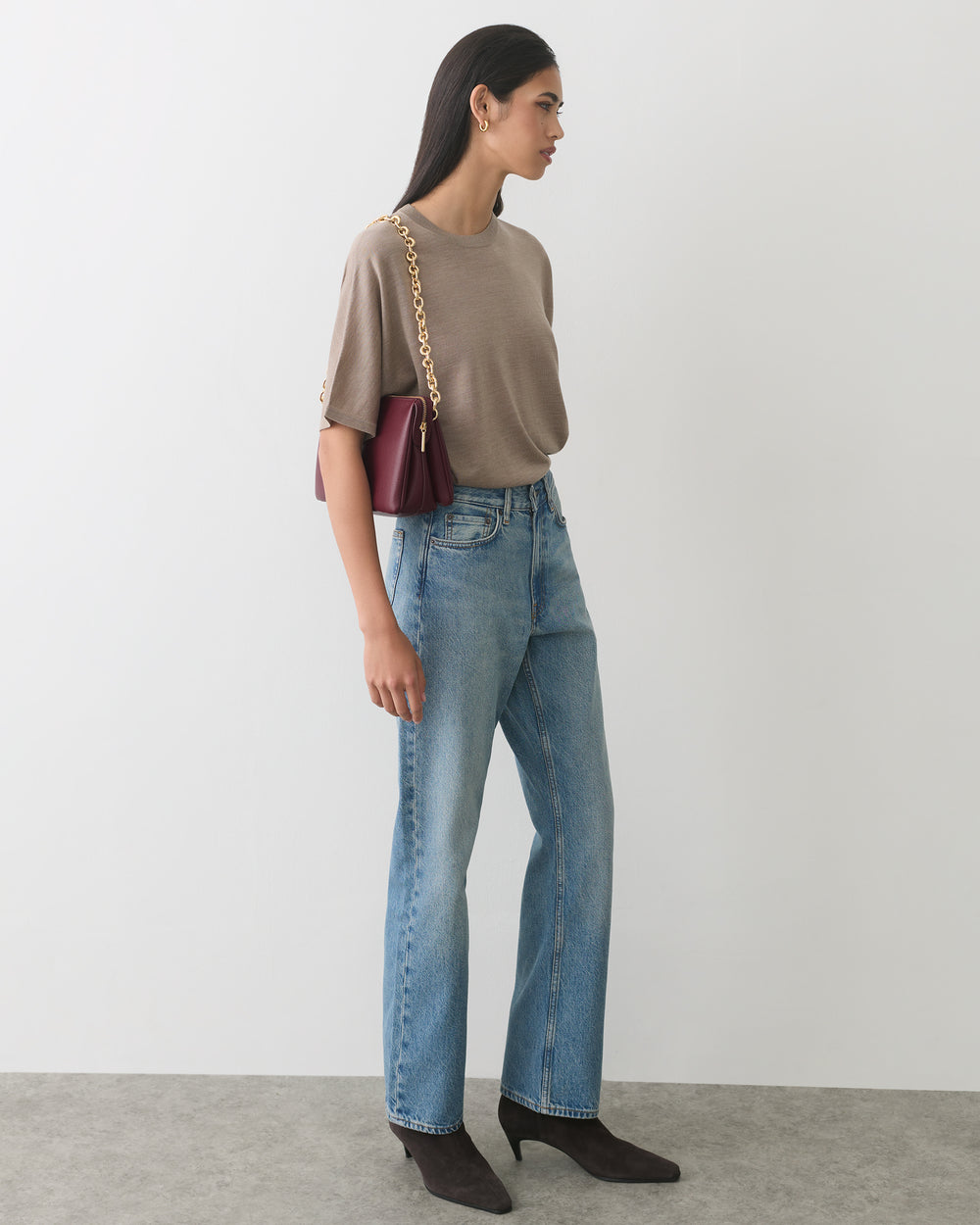 Person wearing a shirt and jeans, carrying a shoulder bag, standing indoors.
