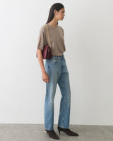 Person wearing a shirt and jeans, carrying a shoulder bag, standing indoors.
