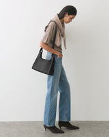 Person standing, wearing casual clothes and holding a shoulder bag.