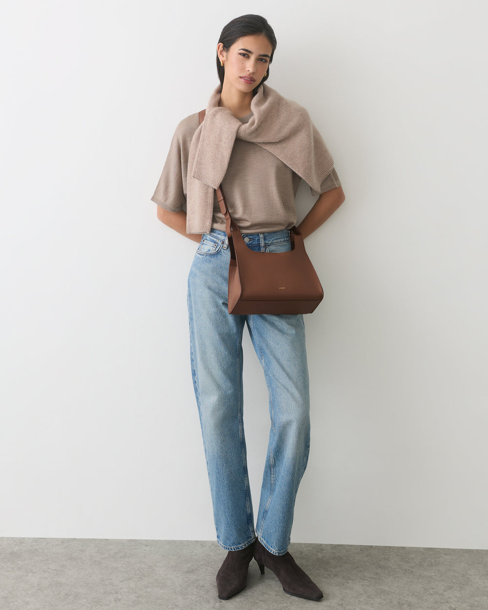 Person wearing jeans and cape with bag on shoulder, standing in a relaxed pose.