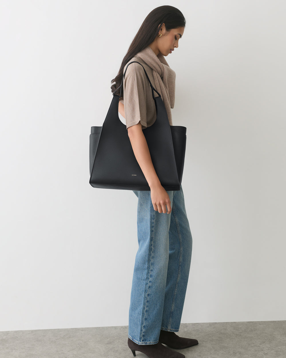 Person with shoulder bag wearing jeans and a top, standing sideways.