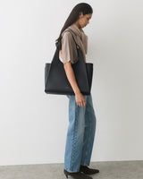 Person with shoulder bag wearing jeans and a top, standing sideways.