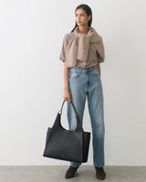 Person holding a large tote bag, wearing a shirt and jeans with a sweater draped over shoulders.