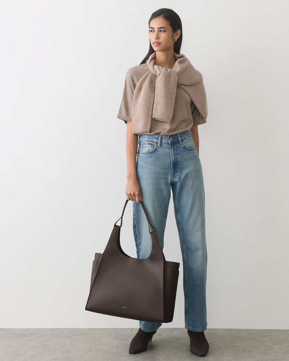 Person holding large tote bag, wearing sweater, jeans, and boots.
