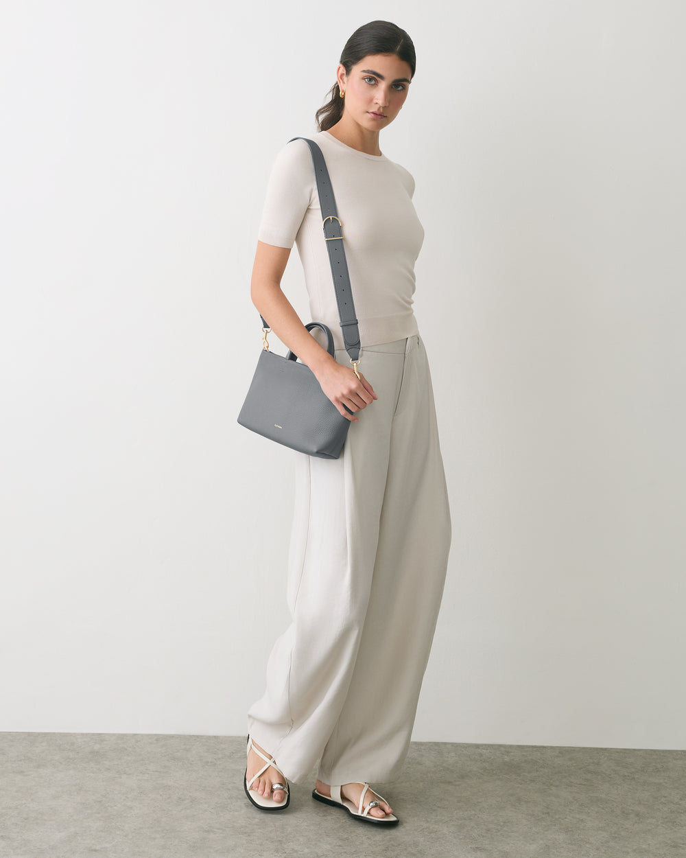 Person standing with a shoulder bag, wearing a t-shirt, wide pants, and sandals.