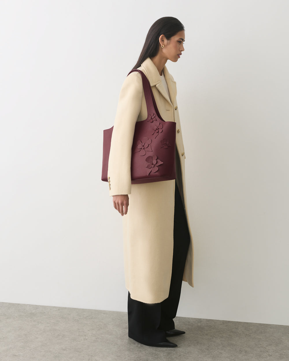 Person in a long coat carrying a tote bag with floral details.